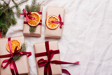 Wrapped gifts with dried orange and velvet pine branches and bows on white linen Christmas decoration diy recipe copy space flat lay top view holiday inspiration