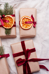 Wrapped gifts with dried orange and velvet pine branches and bows on white linen Christmas decoration diy recipe copy space flat lay top view holiday inspiration