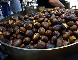 Roasted chestnuts cooked in a large metal pan sold at a street food stall during autumn in the city streets