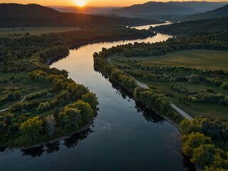 Obraz premium Aerial view of a calm river surrounded by hills at sunset.