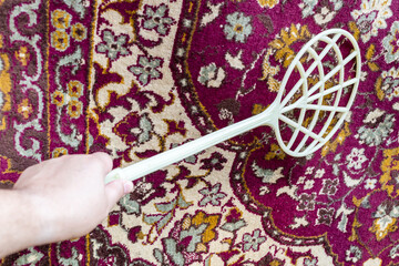 plastic beater knocks dust out old purple carpet