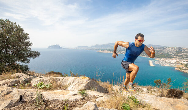 Man trail running on a rocky mountain path with ocean view