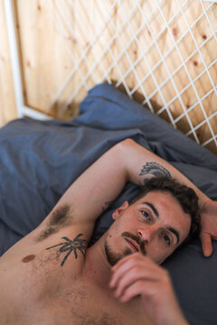 Relaxed man with tattoos lying on bed in cozy setting