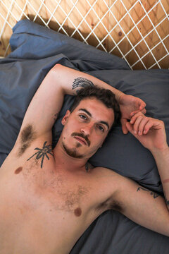 Relaxed man with tattoos lying on bed, looking at camera