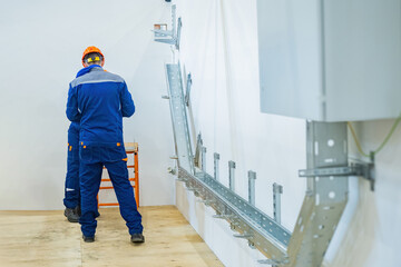 Electricians at work indoors. Two engineers install electrical equipment. Workers install cable...