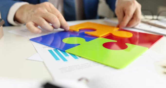 Gentleman in business suit puts piece of puzzle in multicolored square. Businessman shows emblem of company. Concept of team integrity