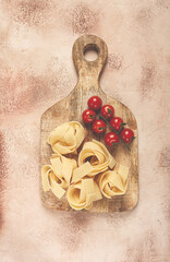 raw pappardelle pasta, on a wooden chopping board, with cherry tomatoes, top view, no people,