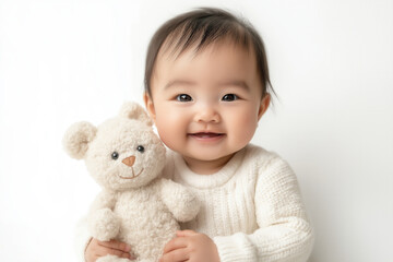 An Asian baby holding a small stuffed animal, sitting on a clean white backdrop with a gentle smile