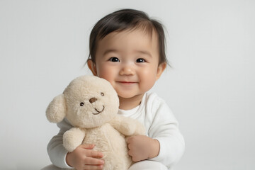 An Asian baby holding a small stuffed animal, sitting on a clean white backdrop with a gentle smile