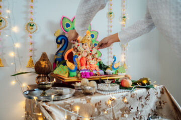 Close up Indian man putting flower garland engages in worship at home altar, adorned with decors and offerings for god Ganesh during festive celebration. Indian culture, hindu ritual and customs.