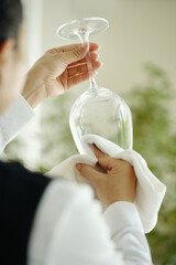 Hands cleaning wine glass with white cloth in bright kitchen setting, ensuring glass is spotless...
