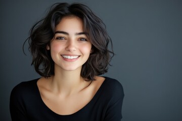 Fototapeta premium A young woman with short, dark hair smiles brightly at the camera. Her expression is friendly and inviting.