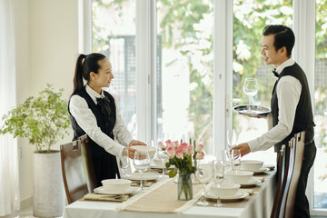 Waitstaff standing prepared at set table with elegant settings in bright dining area with natural light. Coordinated efforts and clear communication ensure seamless service