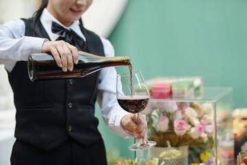 Sommelier pouring red wine into glass, showcasing expertise and precision during elegant event with decor in background. Event is sophisticated and beautifully arranged