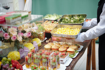Freshly prepared food trays with colorful desserts, mini sandwiches, and vegetables set on a well-decorated table. Flowers and glasses of wine creating an elegant presentation