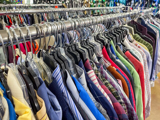 Thrift store clothing rack with selection of preowned secondhand shirts on hangers.