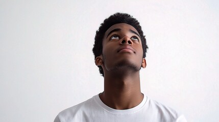 Obraz premium Young Man Looking Upward with Hopeful Expression Against White Wall
