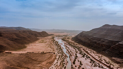 Moroccan Sahara Desert, ancient black volcanic mountains, the Sahara River Oued Ghris, stunning Acacia trees, wild camels, and desert camp,  landscape where golden sand dunes merge with green plants