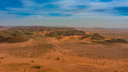 Moroccan Sahara Desert, ancient black volcanic mountains, the Sahara River Oued Ghris, stunning Acacia trees, wild camels, and desert camp,  landscape where golden sand dunes merge with green plants