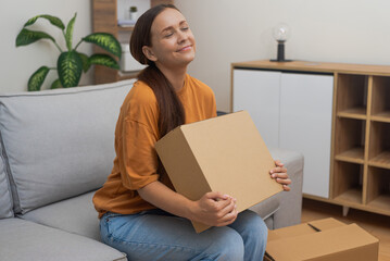 A lady on her couch, embracing a package from an online purchase, appreciating the convenience of home delivery. 