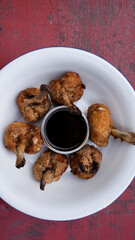 Top view of deep fried breaded chicken wings with a bittersweet dipping sauce, in a white bowl on the red wooden table.