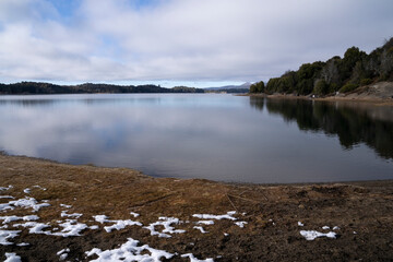 Tranquil environment. Panorama view of the serene lake, forest and mountains in the horizon under a blue sky with clouds. View of the landscape reflection in the ater surface