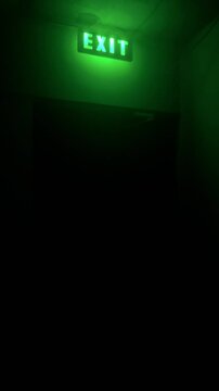 Vertical 4K video. Glowing inscription. Fire exit sign in house. Green light. Concept of emergency, problem solving, trip, fear, horror, gestalt psychology. Hotel. Entrance door. Led lamp. Copy space