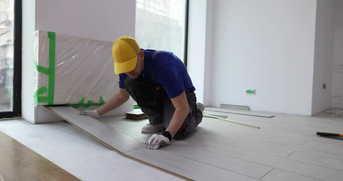 Man carpenter puts wooden boards flooring in house. Male worker aligns long-lasting laminate floor finishing apartment renovation process