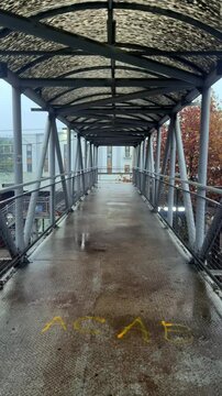 Vertical street 4K first person video. POV. Overground pedestrian crossing in Tbilisi. Old rusty metal corridor with dirty roof. Rain, puddle. Bridge walk. Business center, factory with pipe. City