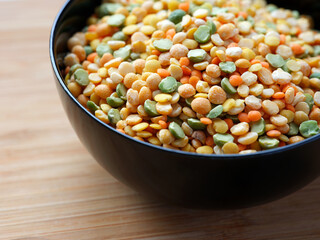Various colorful split legumes in a black bowl on a wooden table. (peas, lentils). Close up.
