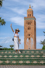 Young Dark Haired Woman in White Dress and Straw Hat with Koutoubia Mosque Tower in the Background