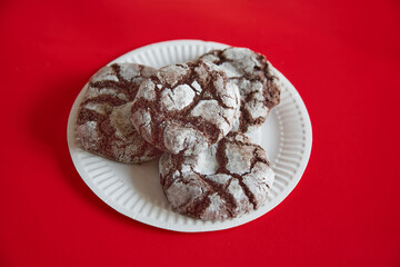 Cracked chocolate cookies on a white paper plate against a red background, close-up, chocolate cookies, treats on a plate.