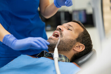 A patient is seated in a dentist's chair with a focus on care and hygiene, receiving careful...