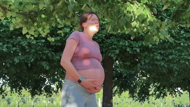 beautiful pregnant woman in 3rd trimester feels unwell outside, in the park in summer, lower back pain and hot