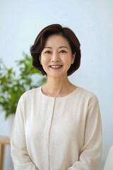 Smiling asian mature female in white blouse in bright room with plants