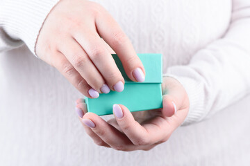 Women's hands with beautiful manicure open a green gift box.