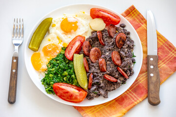 Rustic, nutritious Brazilian food, black bean stew with eggs, grilled sausage, pickles and natural fermentation, kale and vegetables. Real food