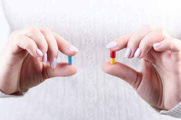 Female fingers hold blue and red-yellow medical capsules.