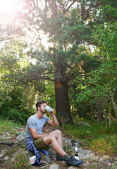 Fototapeta premium Nature, caffeine and man on hike in forest on break for workout, adventure or hobby outdoor. Journey, fitness and male athlete on trekking trip in woods drinking coffee for energy on travel holiday