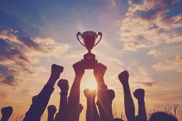 Fototapeta premium Teamwork success holding trophy in sunset silhouette.