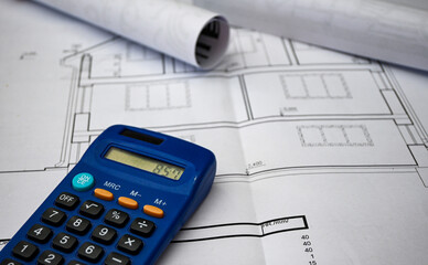 Blue calculator placed on top of rolled-up blueprints depicting house layout, signifying...