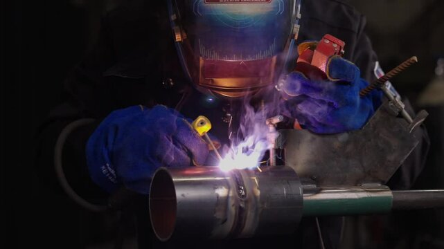 Skilled welder fuses metal pipes with precision, igniting bright sparks and smoke. This dynamic 4K video captures the intensity and artistry of welding in action.