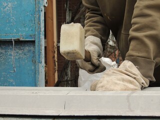 worker with mallet swinging over piece of grey uneven metal to straighten material, working with soft hand hammer to straighten sheet of thin iron