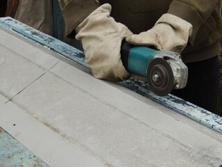 Hands in canvas gloves holding a grinder over a sheet of iron, sawing metal in an outdoor workshop in a village
