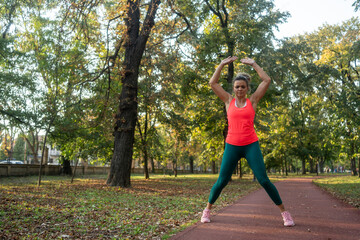 A mature, fit woman and man doing jumping jacks in a city park during summer, enjoying an active...