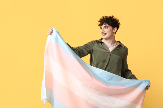 Young transgender woman with flag on yellow background