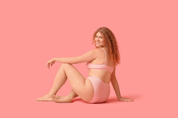 Beautiful young happy body positive woman in trendy underwear sitting on pink background