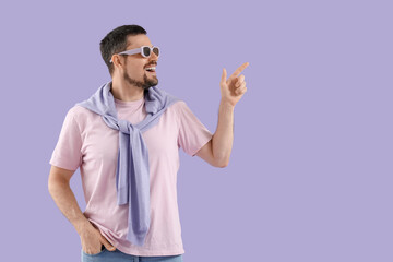 Handsome young man in sunglasses pointing at something on purple background