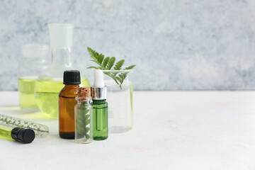 Bottles of oil, laboratory glassware with samples and ingredients for preparing natural cosmetics on white table near grunge wall