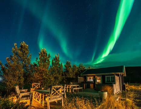 Night time image with northern lights and stars over small cosy cabin with terrace and hot tub